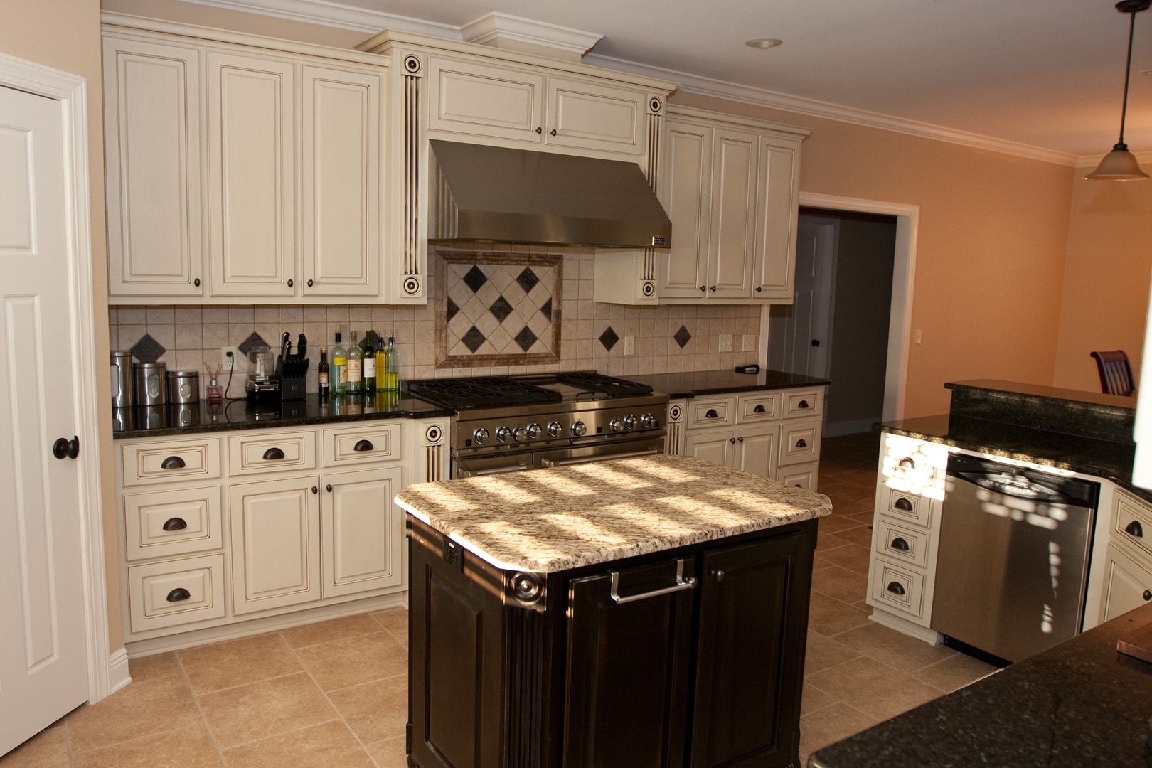 Kitchen island close-up with light granite top, cream glazed cabinets and stainless pro range