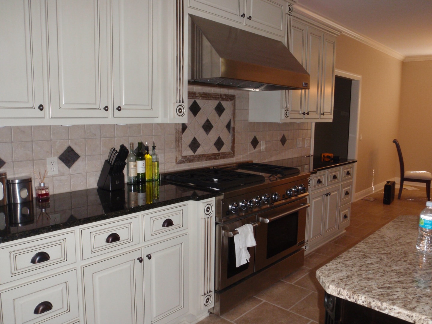 Kitchen range wall with cream glazed cabinets, pro range, diamond tile backsplash and black granite