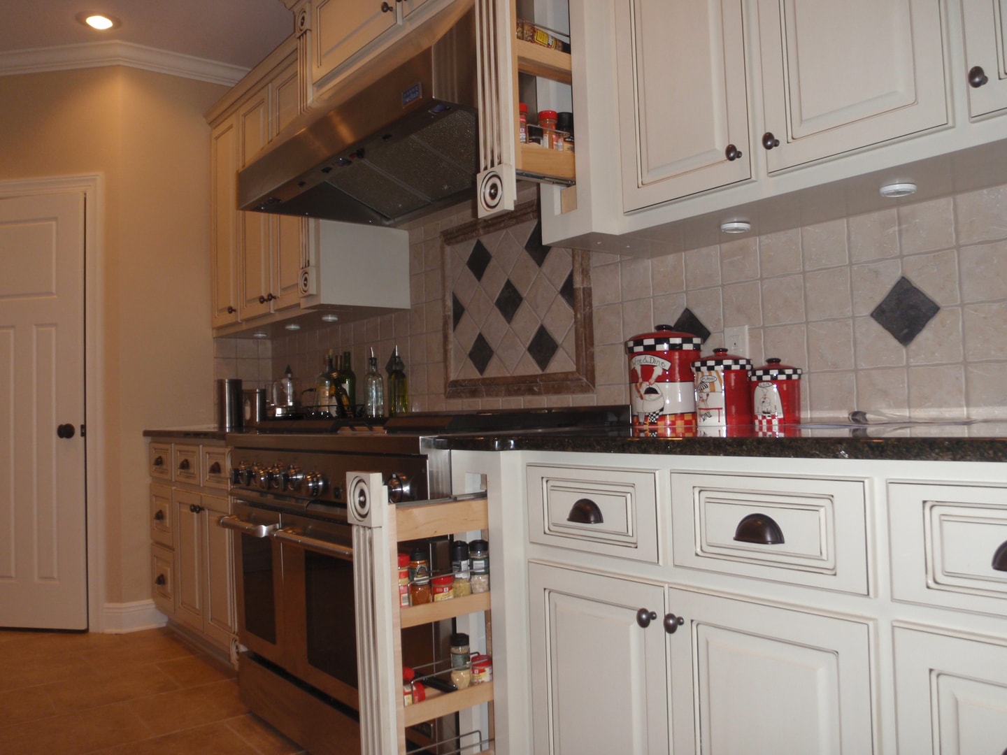 Kitchen pull-out spice rack beside range with cream glazed cabinets and black granite counters