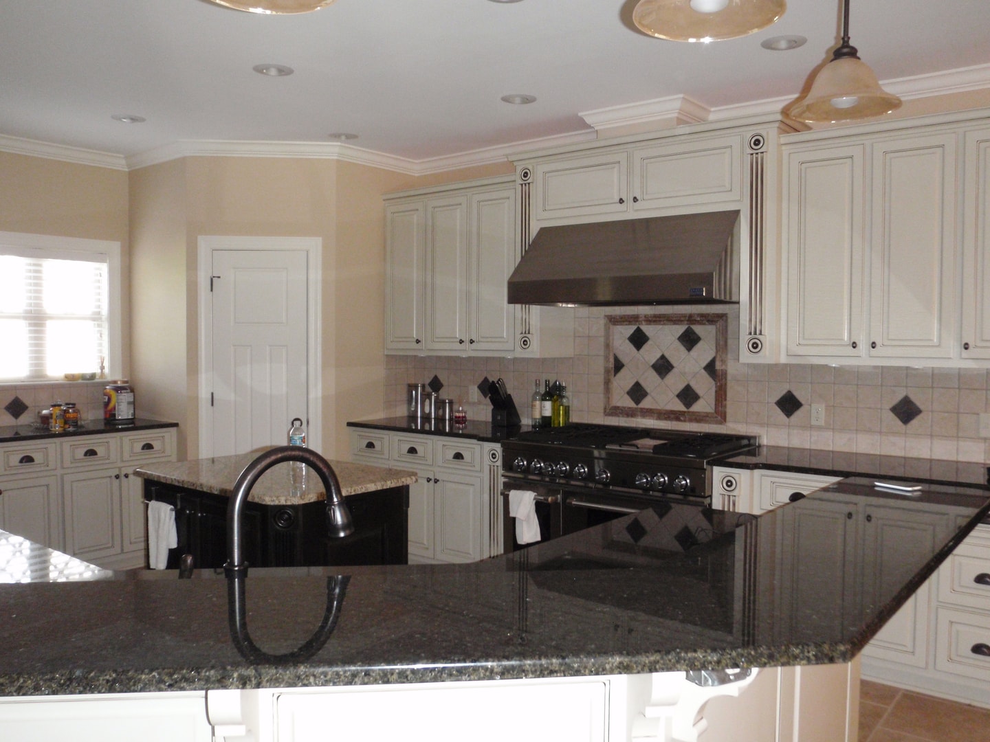Wide angle view of kitchen with cream glazed cabinets, black granite, dark island and pendant lights
