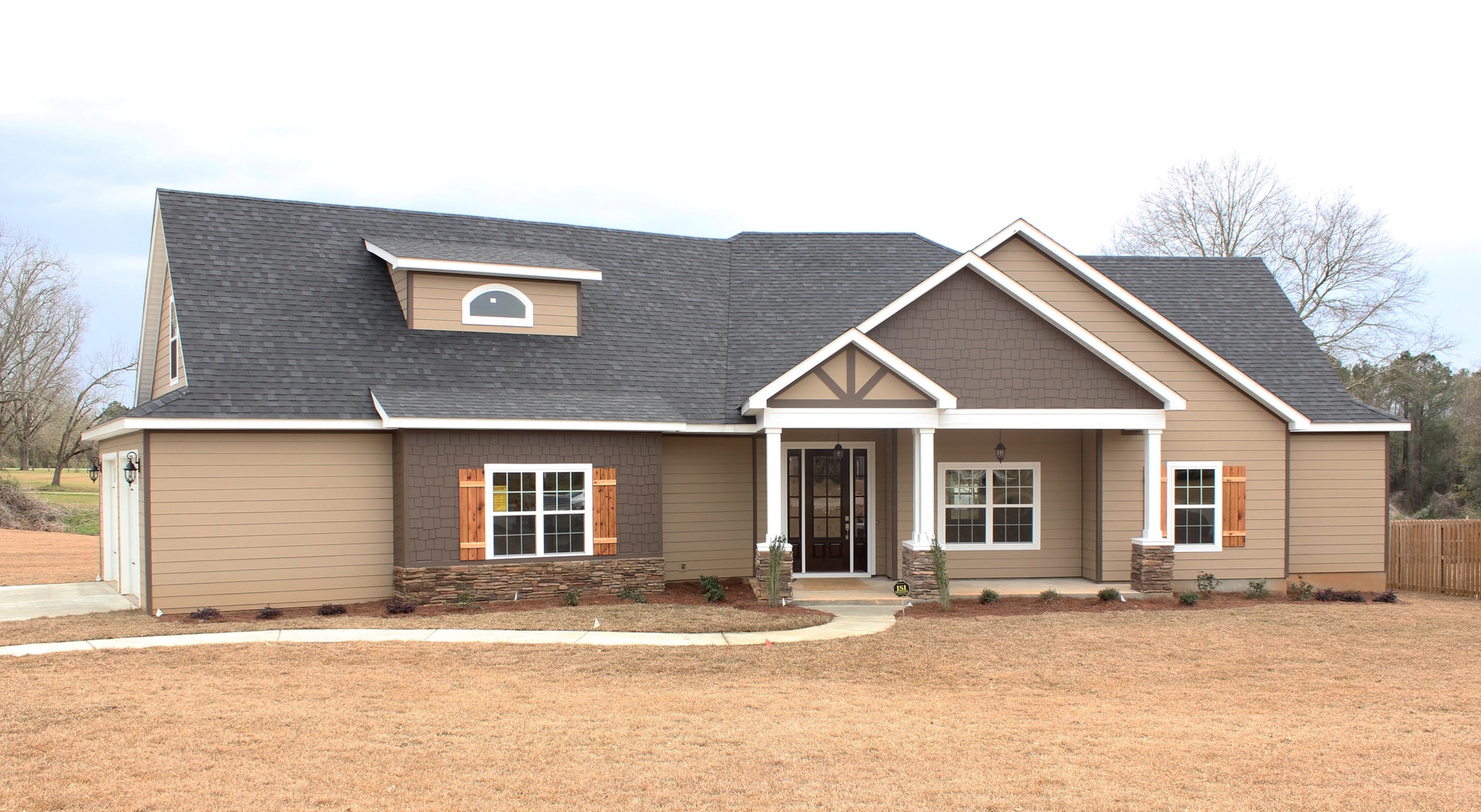 Craftsman ranch home with tan fiber cement siding, cedar shutters, stone base, covered porch with white columns and dark gray roof