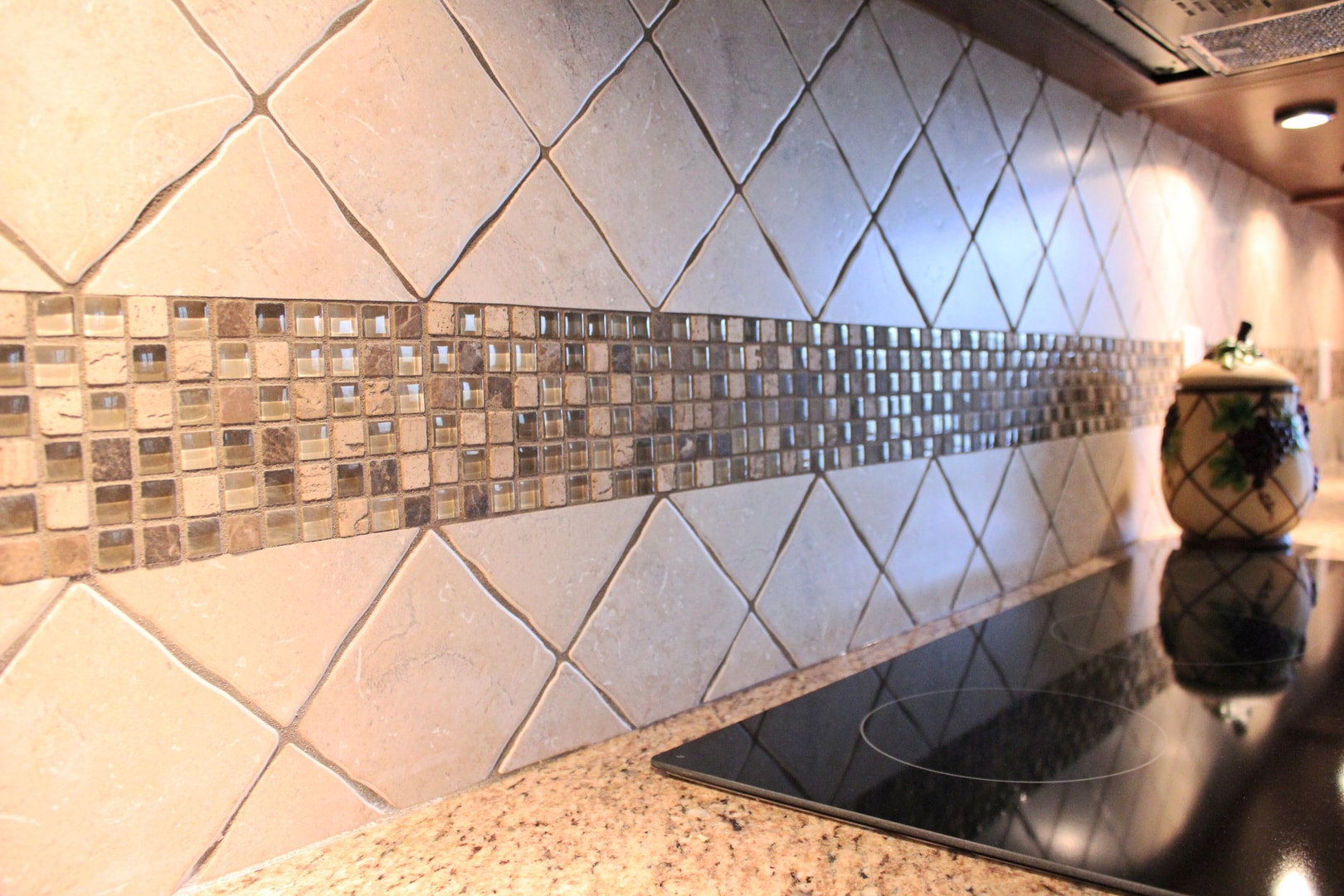 Kitchen backsplash with travertine diamond-set tile, glass and stone mosaic accent strip, black ceramic cooktop and granite counter