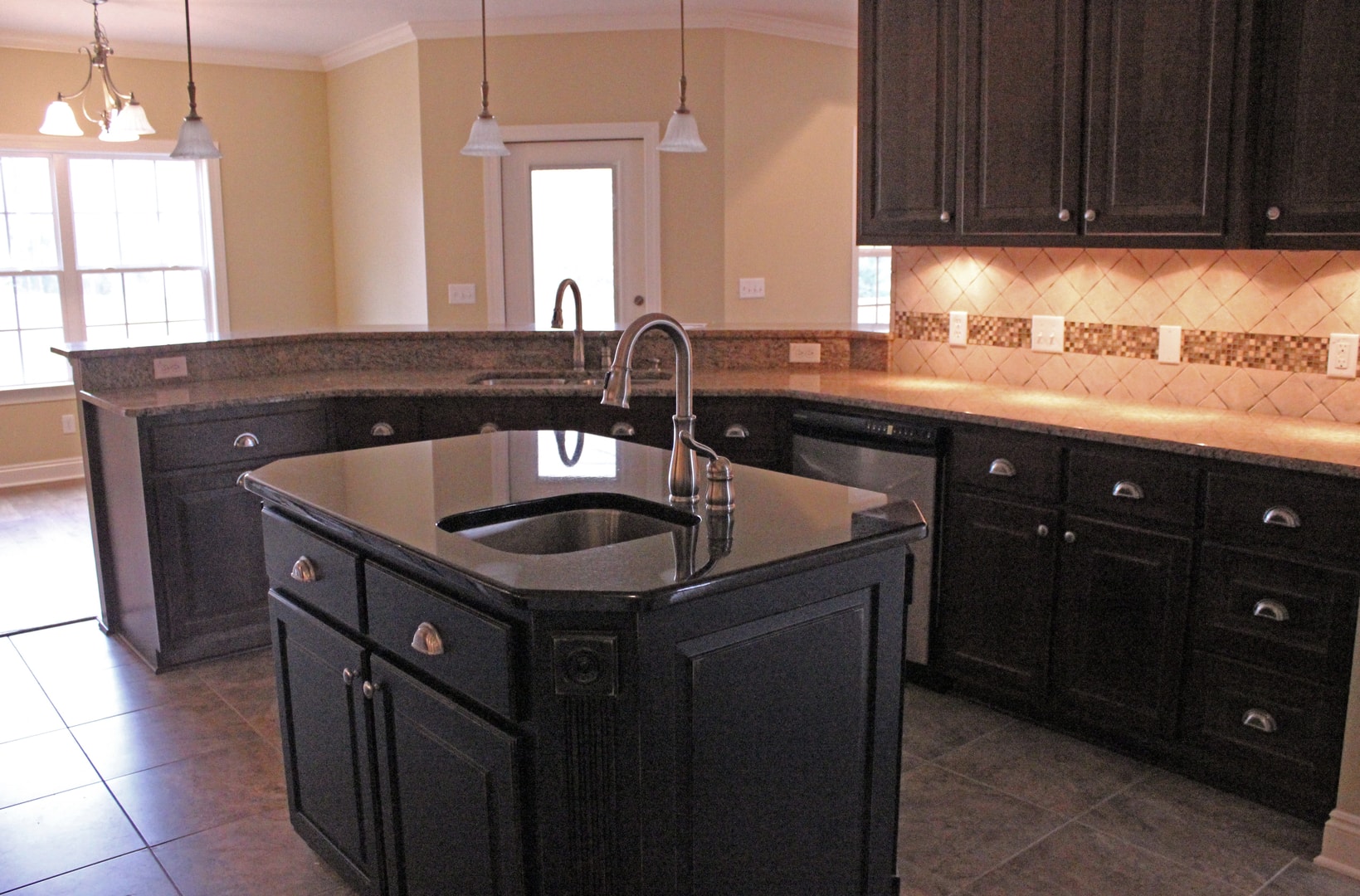 Kitchen with dark espresso cabinets, black granite island with undermount sink, gooseneck faucet, pendant lights and tile floor