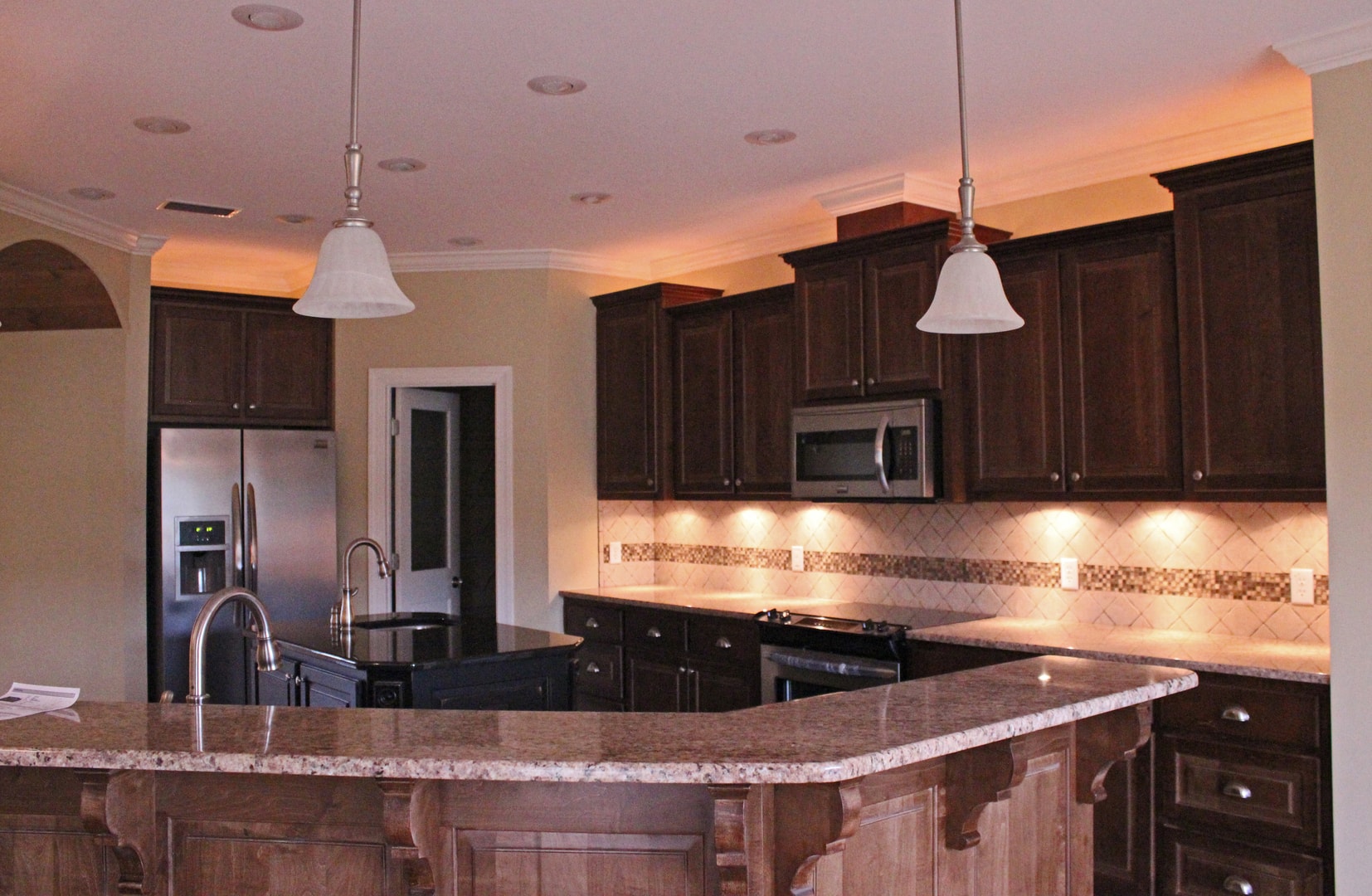 Kitchen full view with dark espresso cabinets, stainless appliances, diamond tile backsplash, curved granite peninsula with corbels and pendant lights