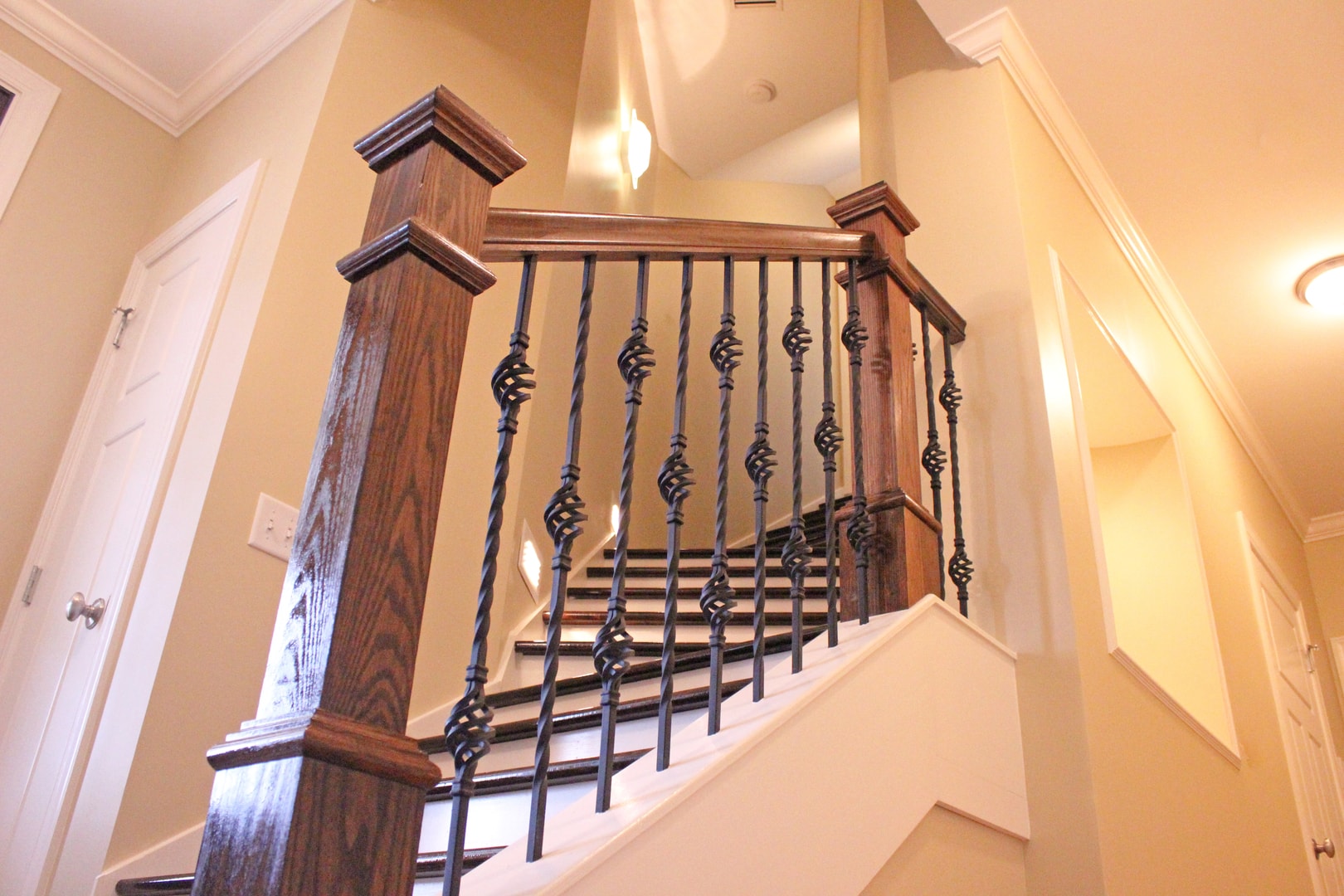 Dark oak newel post with ornate twisted iron balusters featuring basket detail, white risers and crown molding