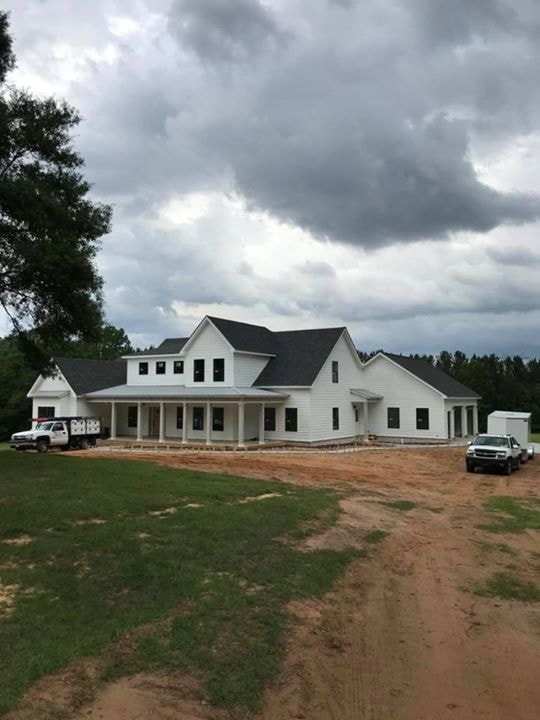 White farmhouse under dramatic storm clouds with Dryden trucks on site