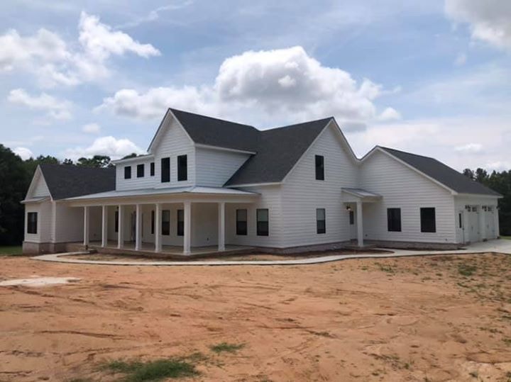 White farmhouse with wraparound porch and dark roof under blue sky