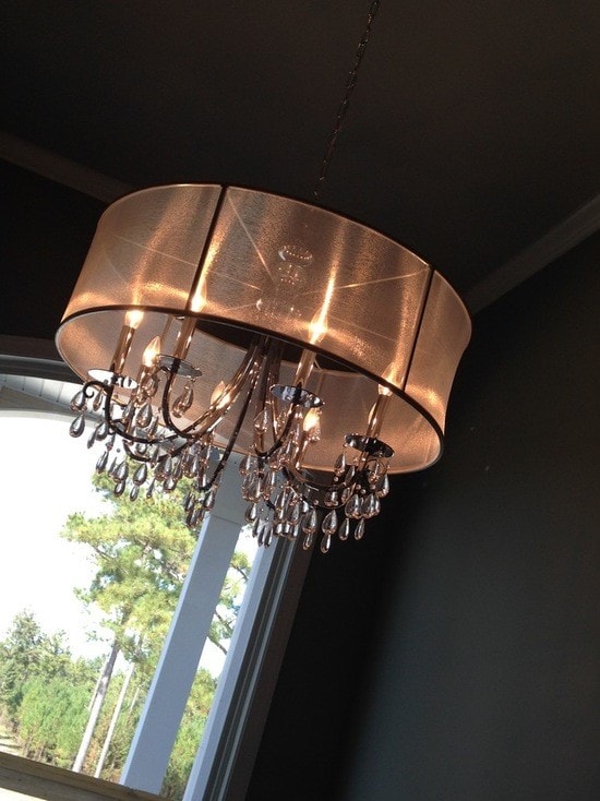 Copper drum pendant chandelier with crystal drops, dark ceiling and tall windows with trees