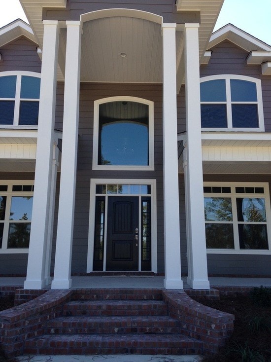Two-story home entry with gray siding, white columns, arched transom window, black door and brick steps