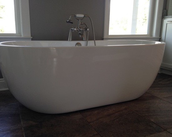 White oval freestanding soaking tub with floor-mount brushed nickel faucet, dark tile floor and tall windows