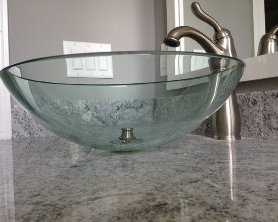 Clear glass vessel bowl sink with brushed nickel faucet on gray granite countertop