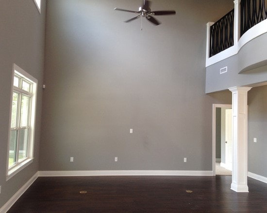 Two-story great room with gray walls, dark hardwood, ceiling fan, ornate loft railing and white columns