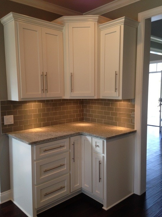 Kitchen corner with white shaker cabinets, bronze subway tile backsplash, gray granite counter and dark hardwood