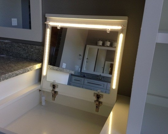Built-in LED-lit vanity mirror with white cabinetry and gray granite counter reflected