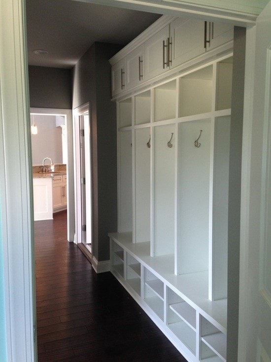 White built-in mudroom locker system with hooks, bench, cubbies and upper cabinets on dark hardwood