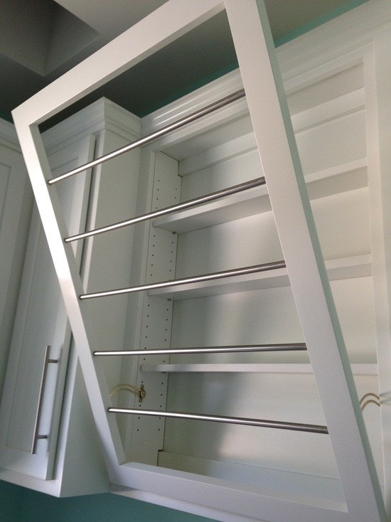 White cabinet door open revealing pull-out stainless steel drying bars with teal walls