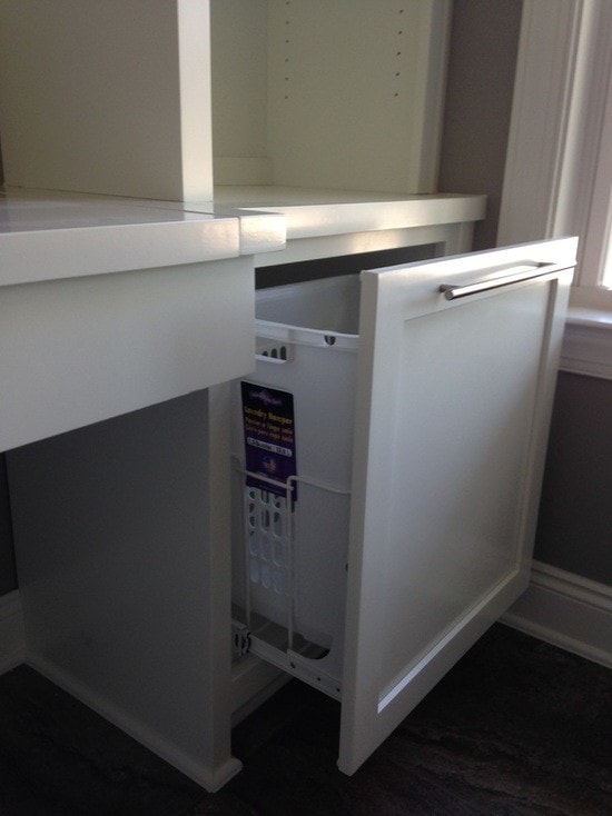 White cabinetry with pull-out laundry hamper drawer on dark hardwood floors