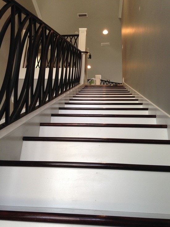 Staircase with dark walnut treads, white risers, black geometric X-pattern iron railing and recessed lighting