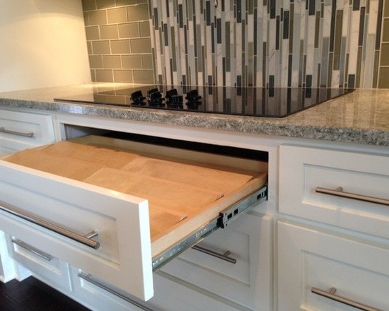 White shaker kitchen with pull-out cutting board drawer under cooktop and glass tile backsplash