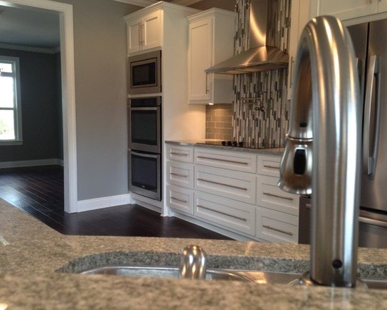 Kitchen from island showing white shaker cabinets, double wall ovens, stainless fridge and glass tile backsplash