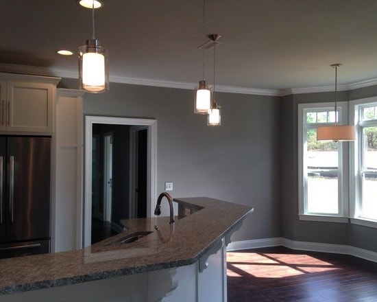 Curved granite island with three pendant lights, gray walls, dark hardwood and bay window
