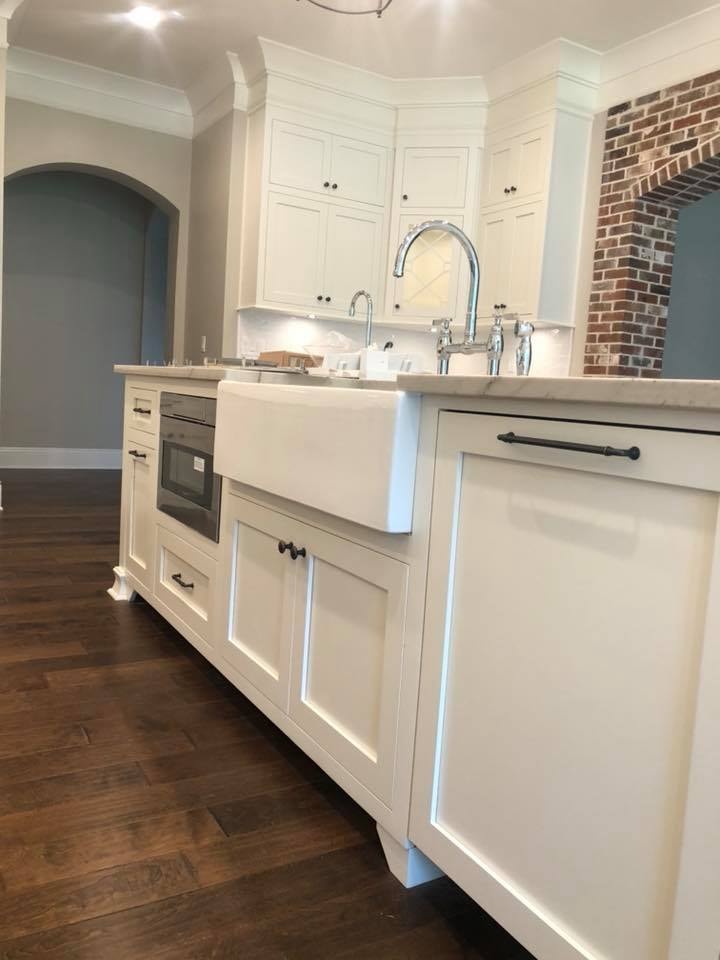 Kitchen island with farmhouse sink, white cabinetry and brick archway