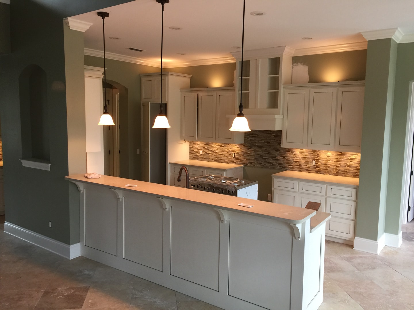 Kitchen with sage green walls, white cabinetry, corbel island, pendant lights and mosaic backsplash