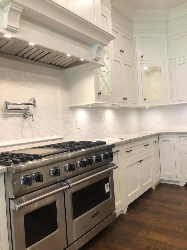 White kitchen with Viking range, herringbone backsplash and custom hood