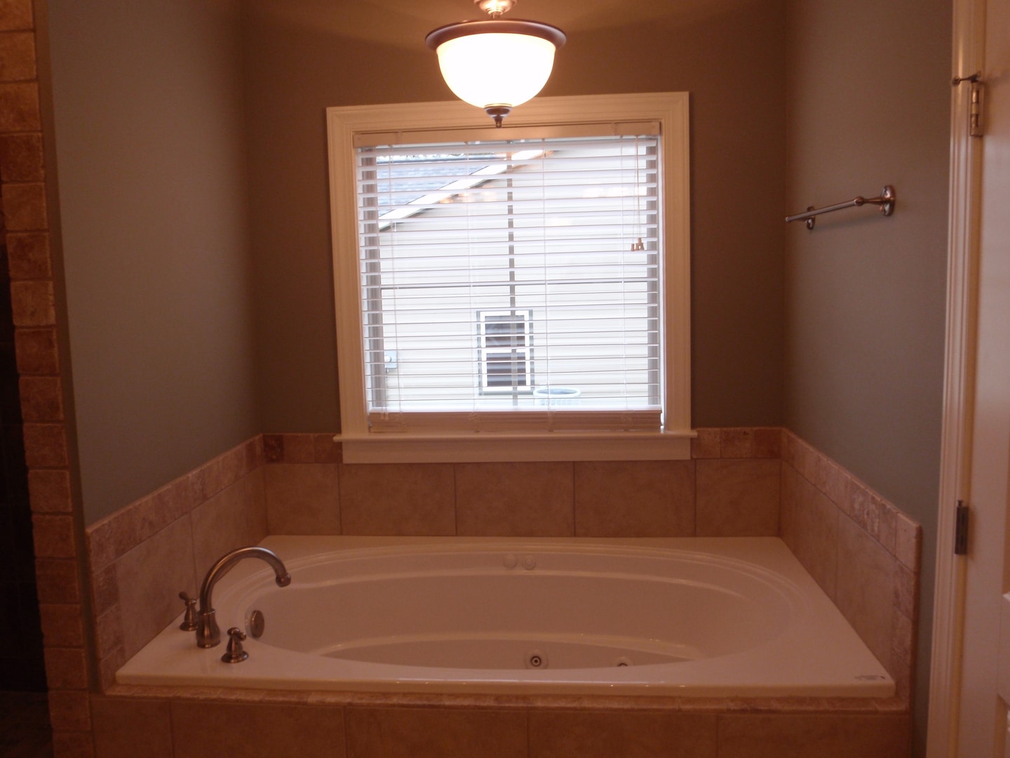 Drop-in soaking tub with travertine tile surround, window with blinds and flush mount light