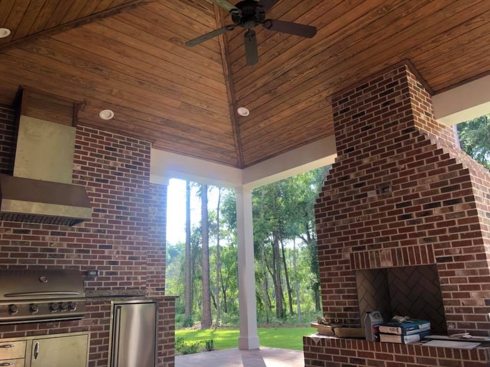 Covered outdoor kitchen with wood ceiling and brick fireplace