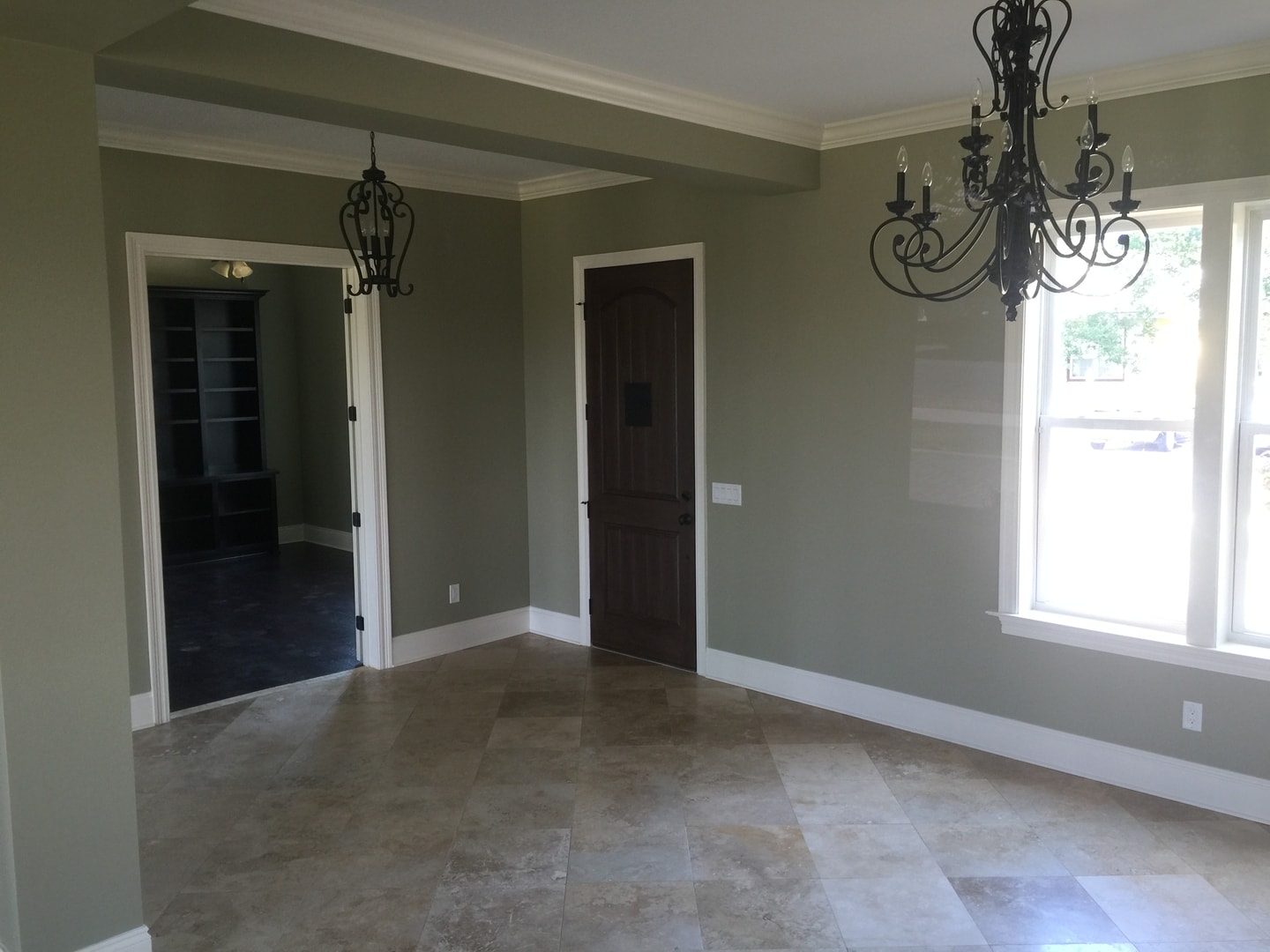 Dining room with sage walls, travertine floor, two wrought-iron chandeliers and arched doorways