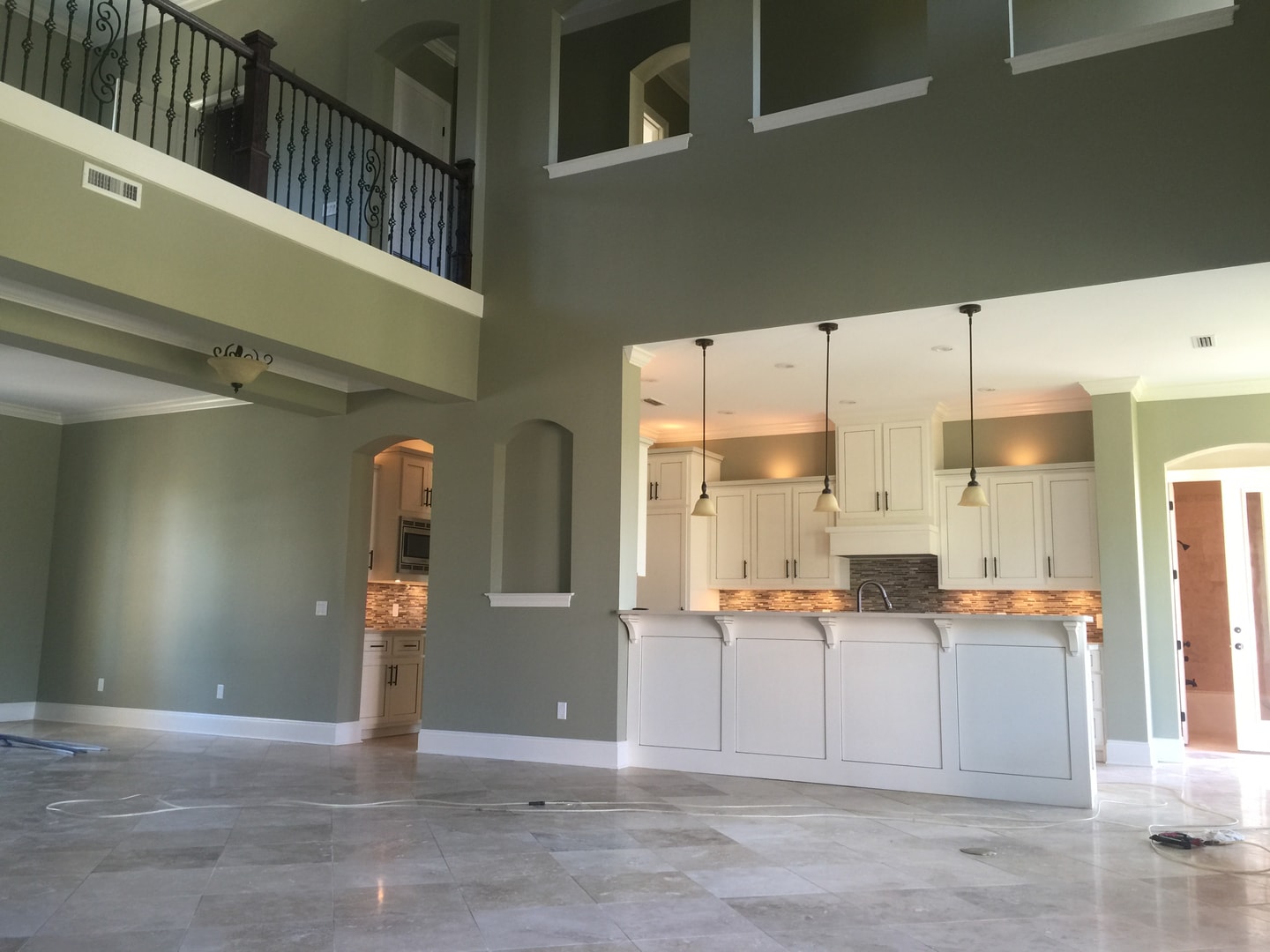 Two-story great room under construction with white kitchen island and wrought-iron loft railing