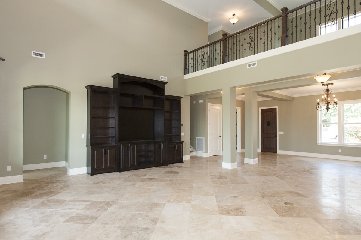 Two-story great room with sage walls, dark entertainment center, wrought-iron loft railing and travertine floor