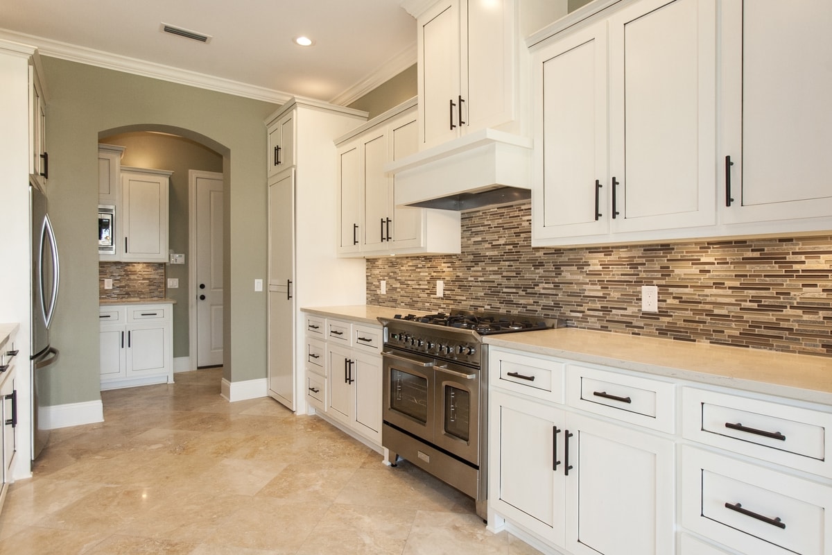 White shaker kitchen with mosaic backsplash, pro range, travertine floor and arched doorway