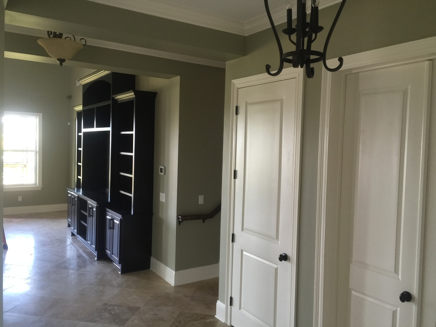 Living room with sage walls, dark entertainment center built-in, wrought-iron chandelier and travertine floor