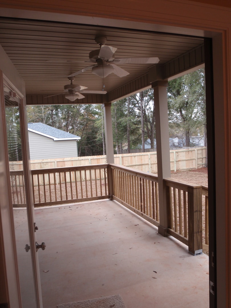 Screened porch with beadboard ceiling, two ceiling fans, wood railings and wooded backyard view