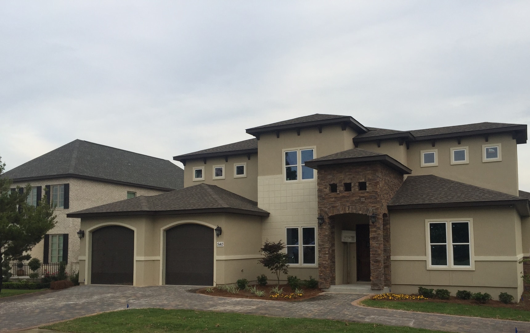 Finished stucco home with stone arch entry, double garage and paver driveway