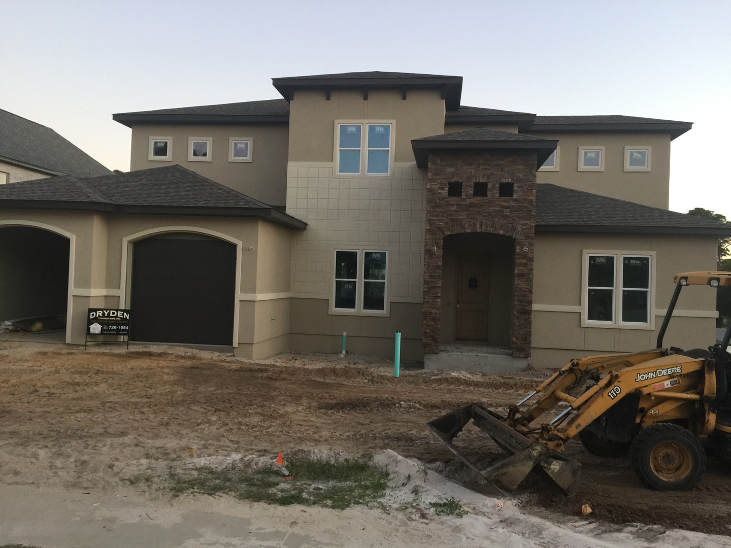 Stucco home with stone arch entry tower and Dryden sign, John Deere backhoe on site