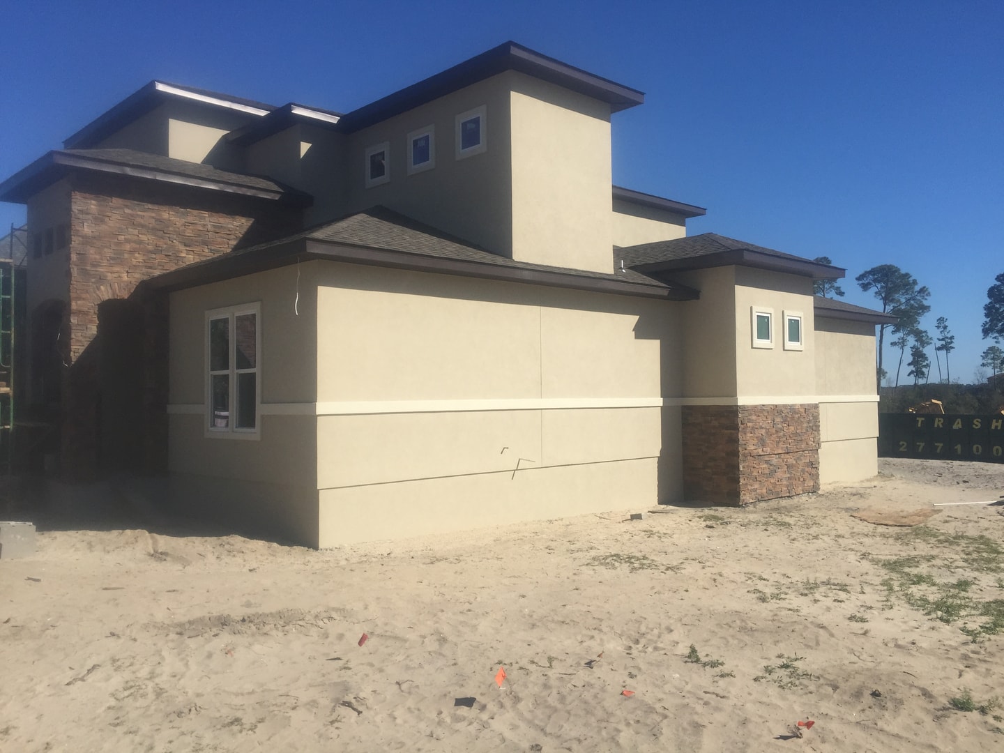 Side elevation of stucco home under construction with stone accent base