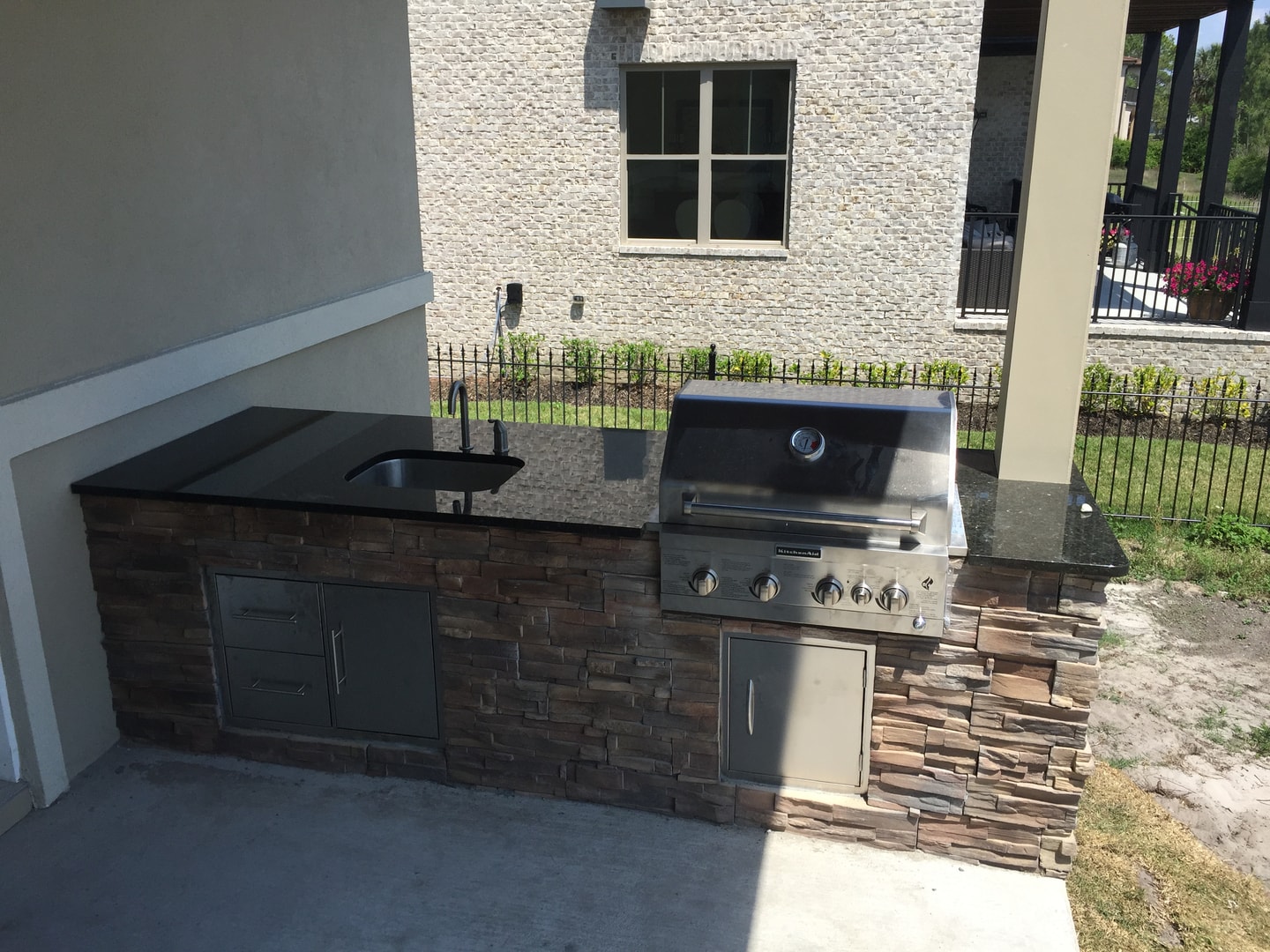 Outdoor kitchen with stacked stone veneer, black granite counter, KitchenAid grill and undermount sink
