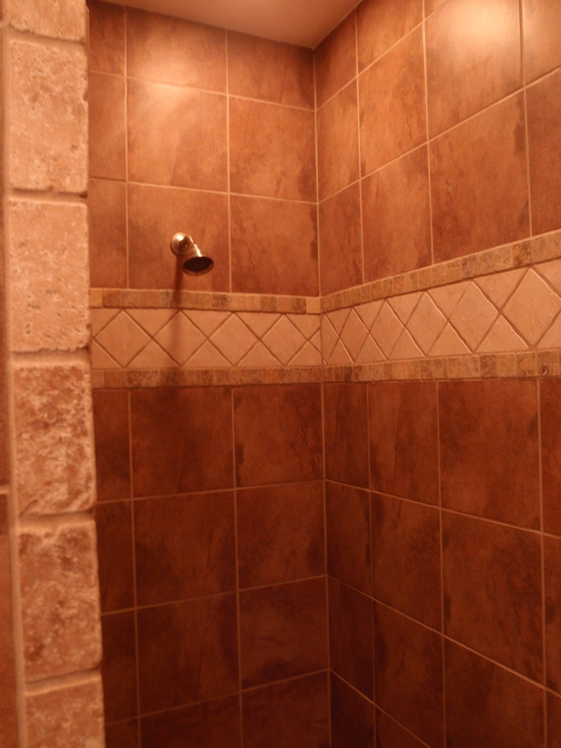 Terracotta tile shower with diamond accent border, stacked stone surround and rain head