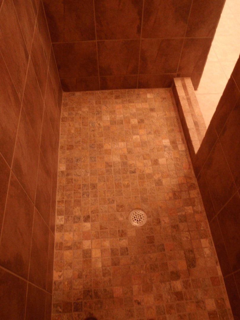 Shower with small square terracotta mosaic floor tile, large format wall tile and corner bench