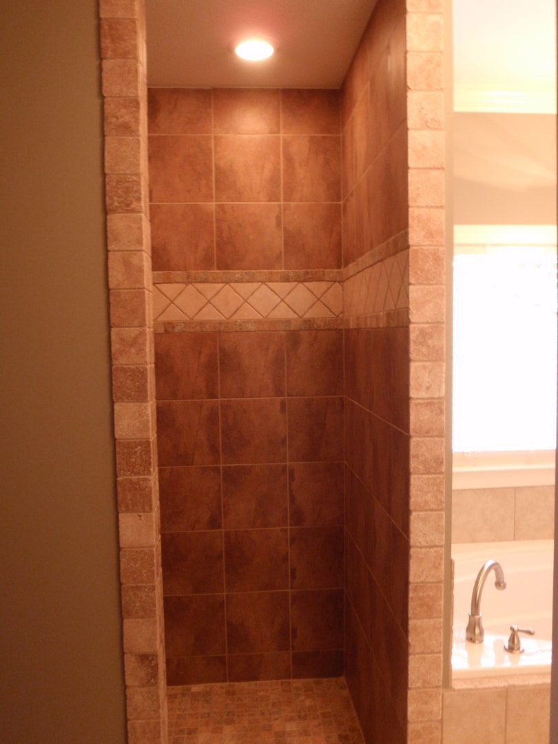Shower entry with stacked stone columns, terracotta tile interior and soaking tub visible at right