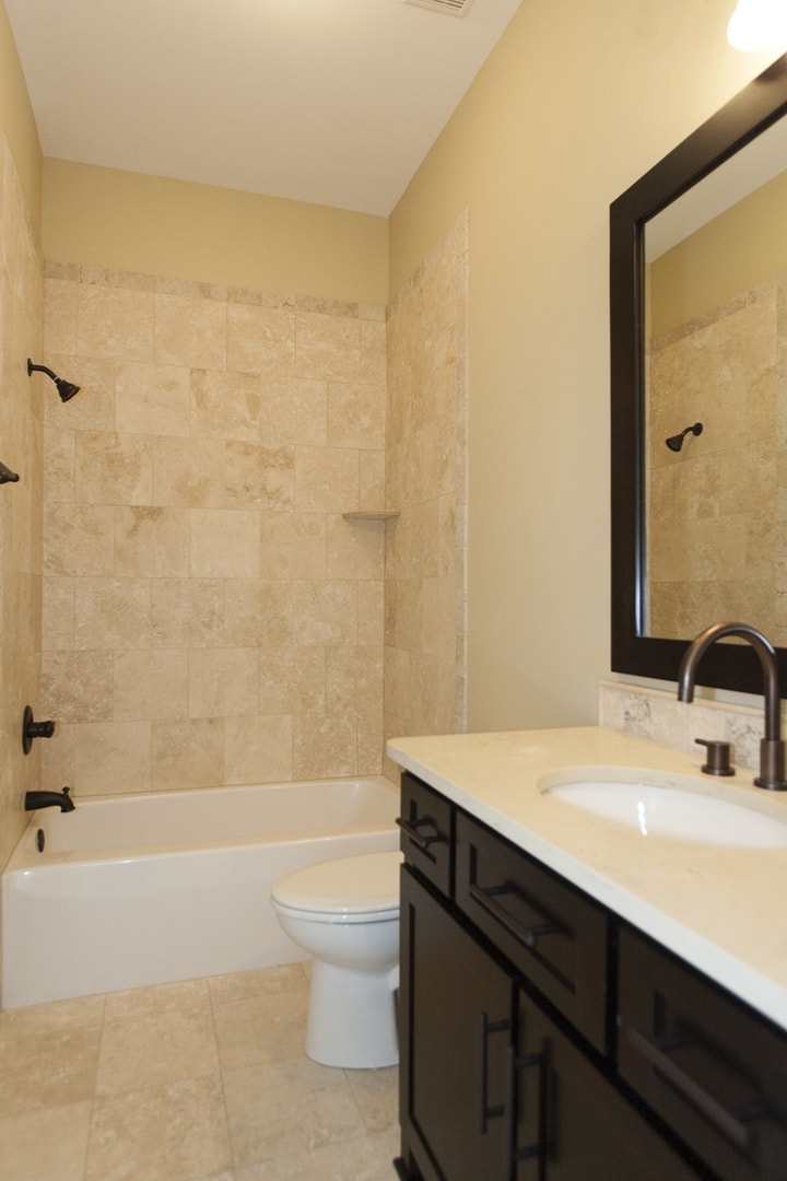 Guest bath with travertine tile surround, dark vanity, oil-rubbed bronze fixtures and quartz counter