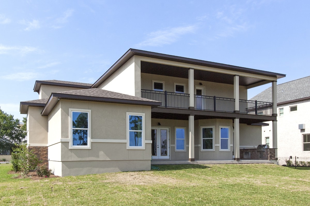 Rear of tan stucco two-story home with upper balcony, black railing and covered lower porch