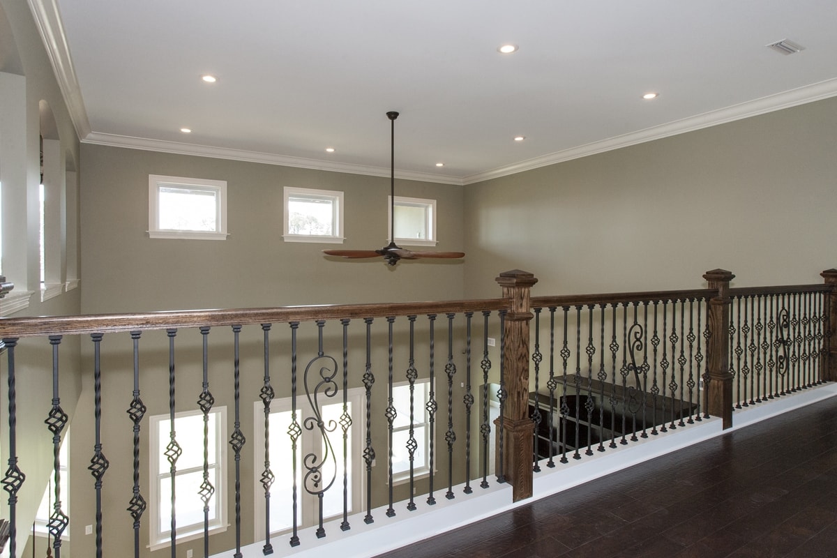 Upper loft hallway with ornate ironwork railing, ceiling fan, recessed lights and dark hardwood
