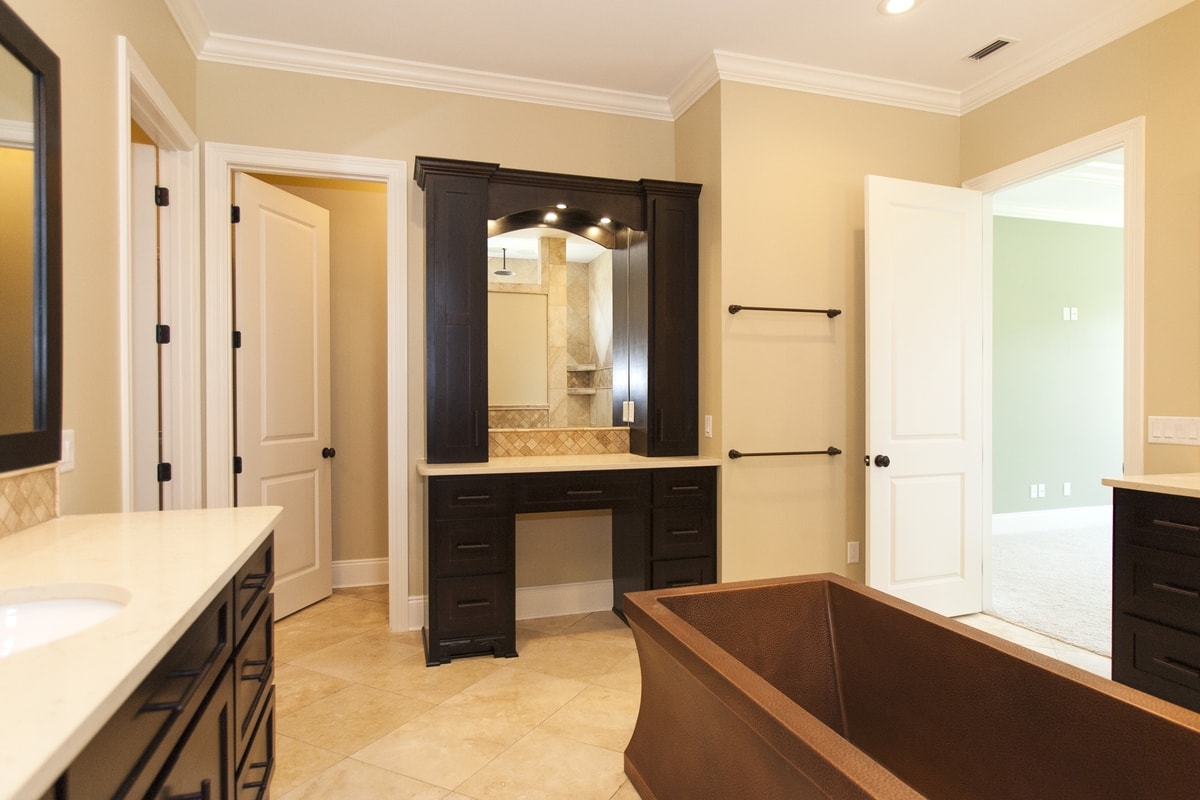 Master bath with dark built-in makeup vanity, lit mirror, hammered copper tub and travertine tile