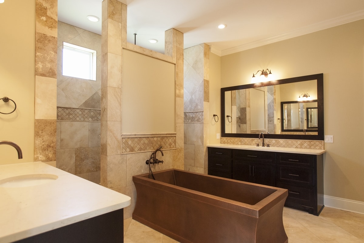 Master bath with hammered copper tub, dark double vanity, travertine tile columns and wall sconces