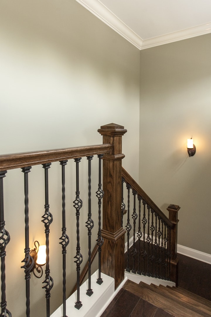 Staircase landing with dark wood newel post, basket-twist iron balusters and wall sconces